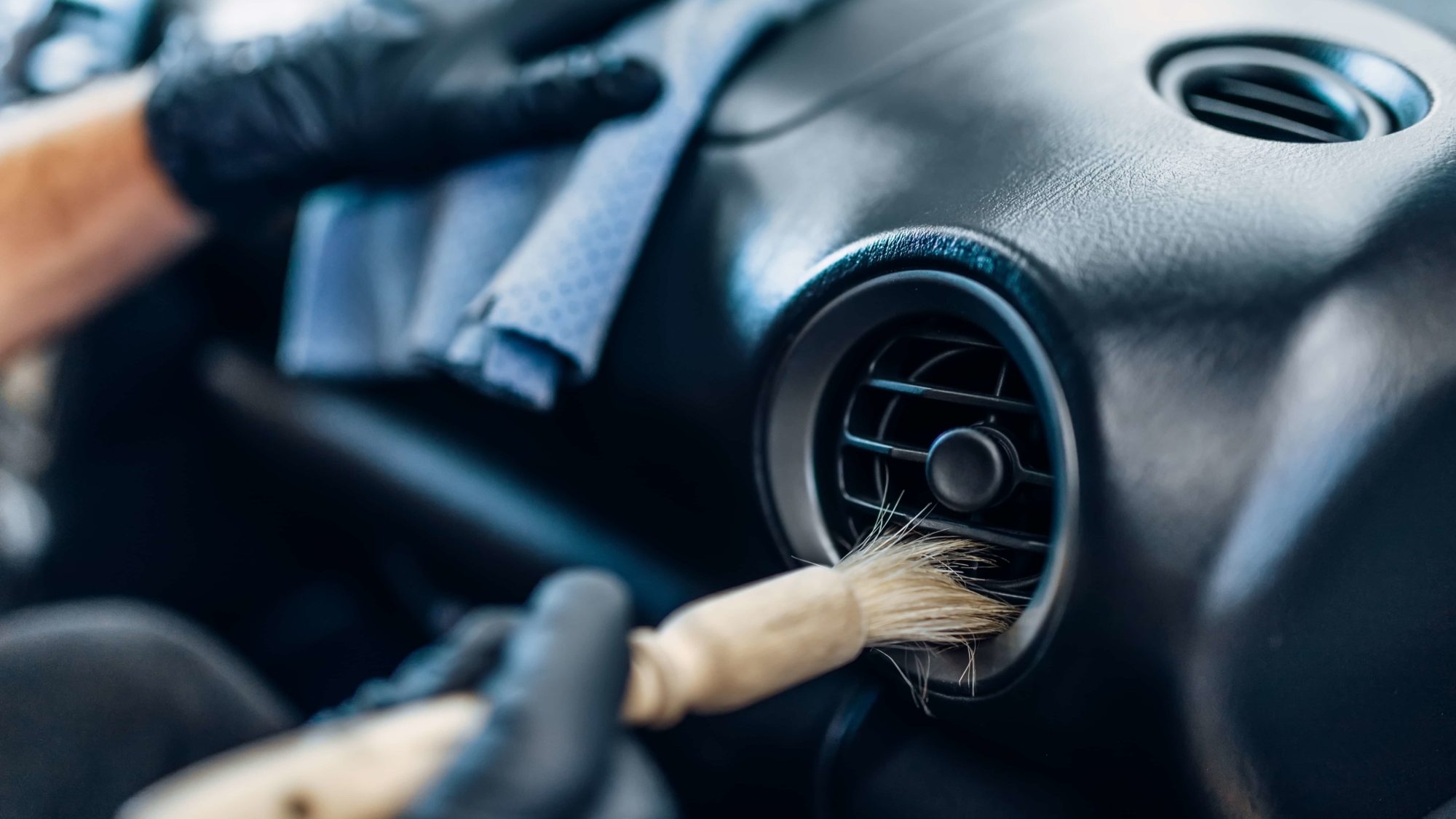 Auto detailing of car interior on carwash service. Worker in gloves cleans salon with brush