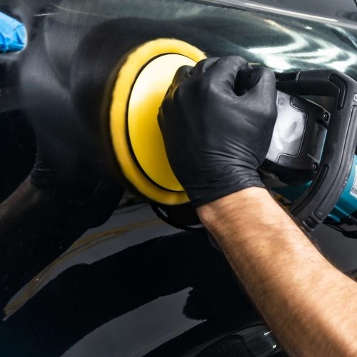 Car polish wax worker hands applying protective tape before polishing. Buffing and polishing car. Car detailing. Man holds a polisher in the hand and polishes the car. Tools for polishing