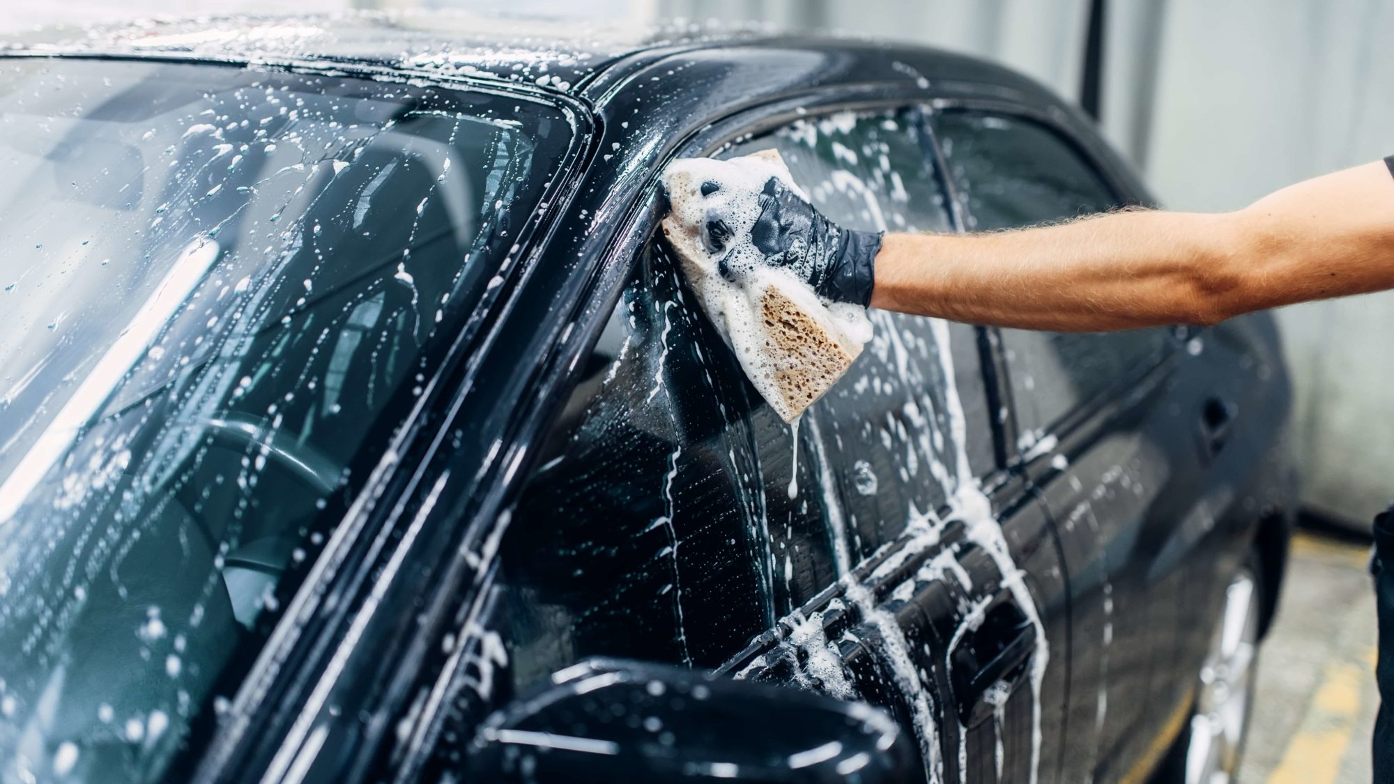 Carwash service, car cleaning, front view. Auto detailing, worker soaps glasses