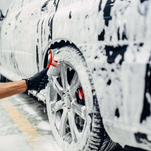 Carwash service, car in foam, side view. Auto detailing, washing of wheels with brush